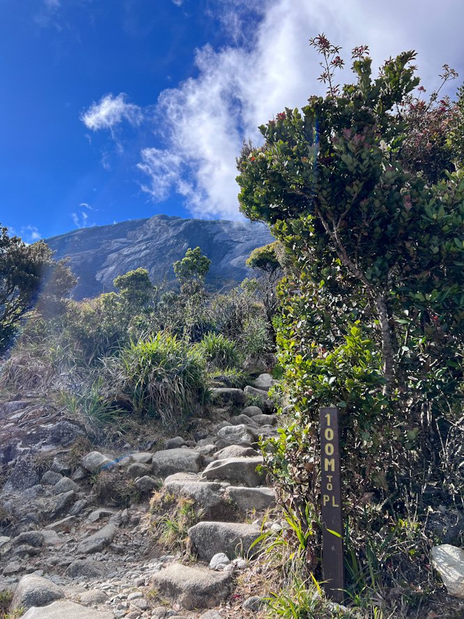 100m to Panalaban Base Camp sign on Mount Kinabalu with steep rocky stone steps and distant granite peaks in Kinabalu Park Sabah