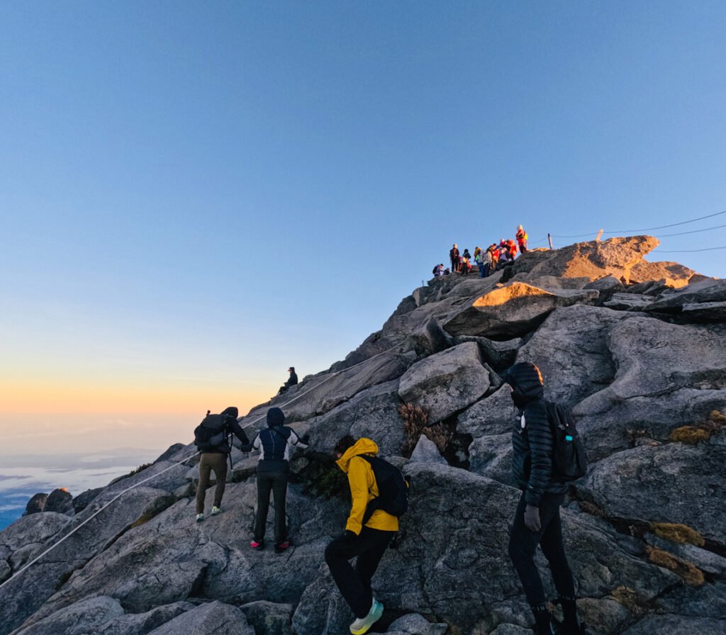 Trekkers climbing steep granite slabs with fixed ropes toward Low's Peak summit on Mount Kinabalu at dawn with sunrise, Sabah Borneo. © SlowingwithT.com